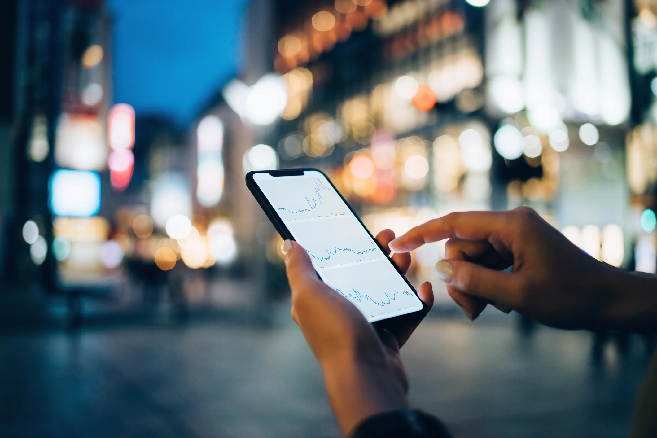 Persoană verificând grafice de active digitale pe telefon, seara, într-un oraș